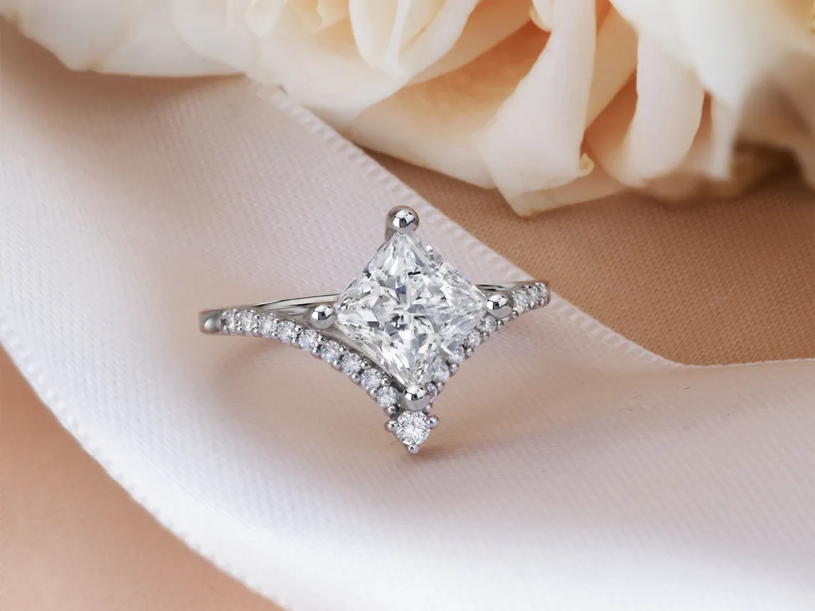 Elegant diamond engagement ring with a princess cut center stone, set on a delicate band. Visit Bryan Jewelry for more.