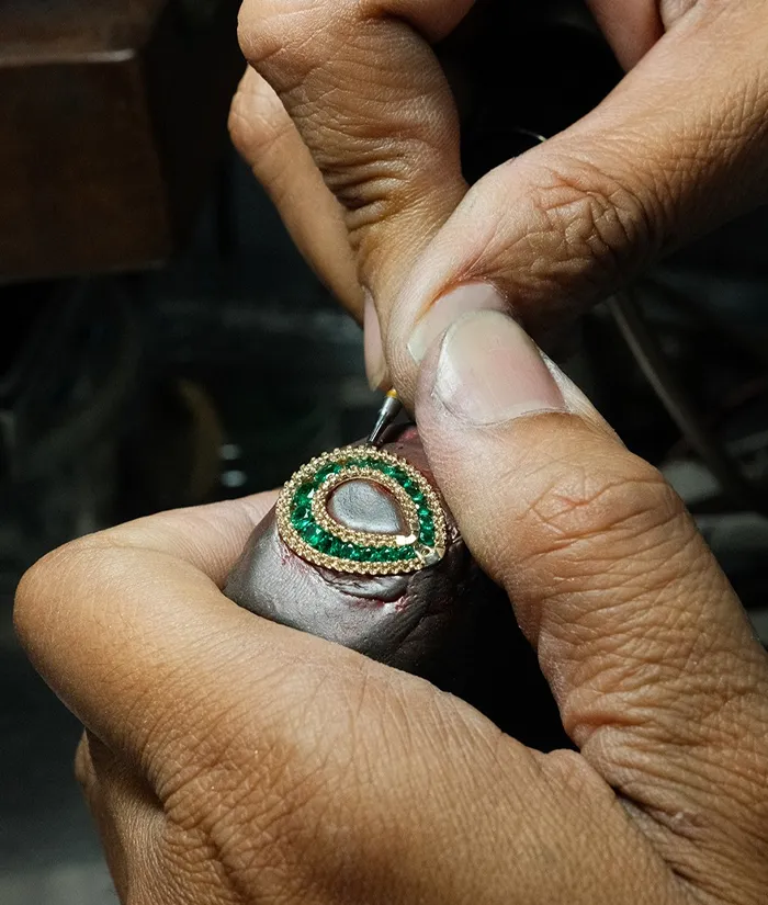 A jeweler meticulously setting green gemstones in a gold ring, showcasing craftsmanship at Bryan Jewelry in Prattville.