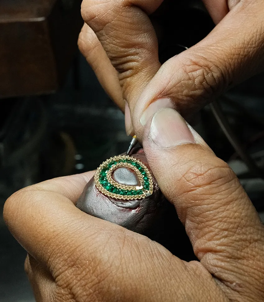 A jeweler meticulously setting green gemstones in a gold ring, showcasing craftsmanship at Bryan Jewelry in Prattville.