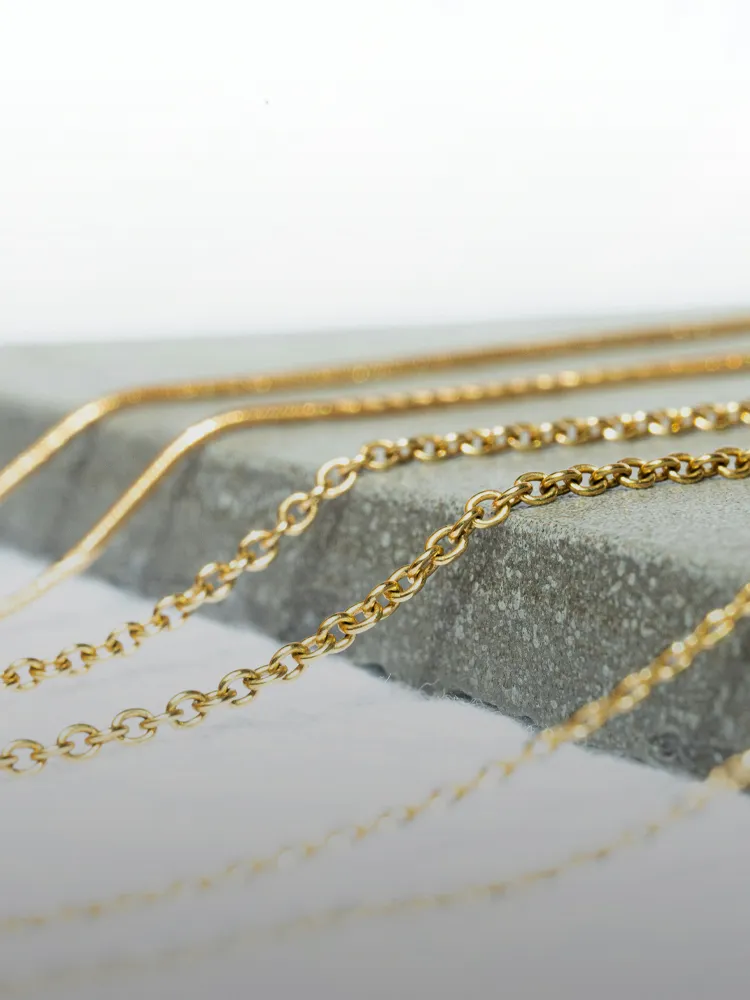 Close-up of gold chains on a stone surface, showcasing various styles for chain and clasp repair at Bryan Jewelry.
