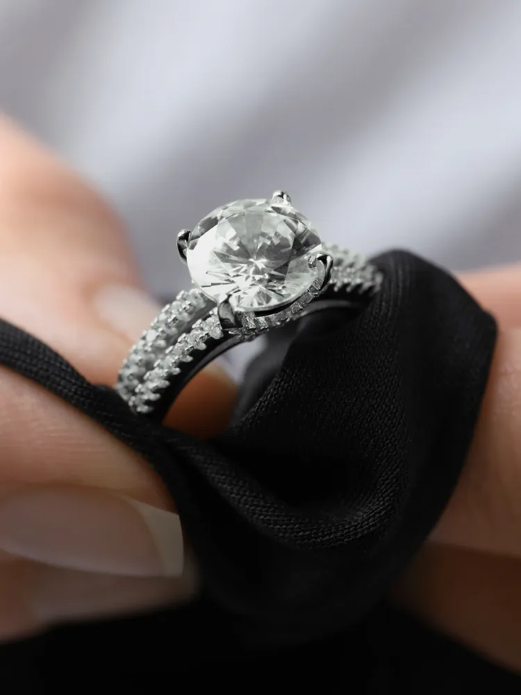 A hand holding a sparkling diamond engagement ring on a black cloth background. Visit Bryan Jewelry for more.