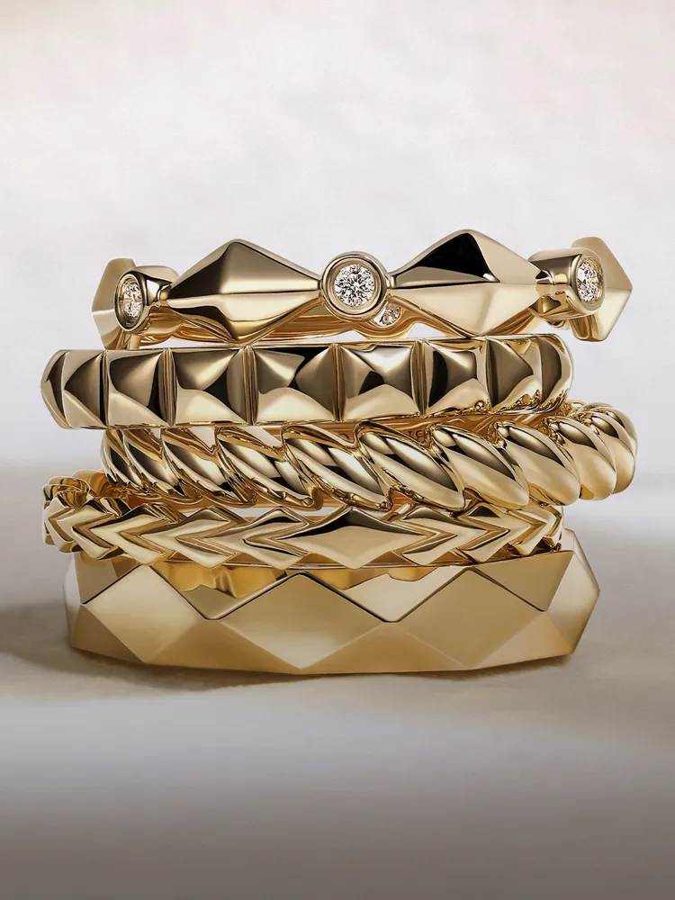 Stack of gold rings with various designs, including smooth, textured, and diamond accents. Visit Bryan Jewelry for more.