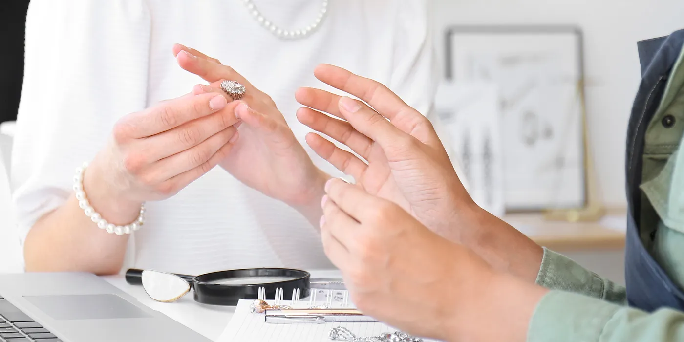 A customer examines a diamond ring with a jeweler in a bright, modern jewelry store setting.