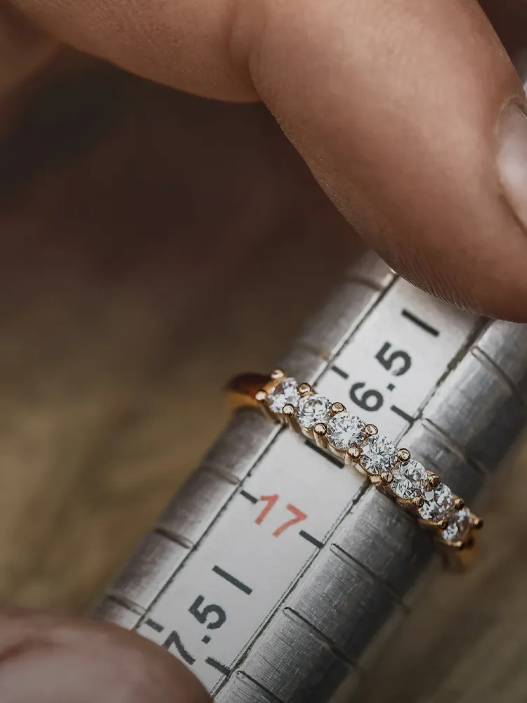 A hand holds a diamond ring on a ring sizer, indicating resizing. Click for jewelry repair services at Bryan Jewelry.