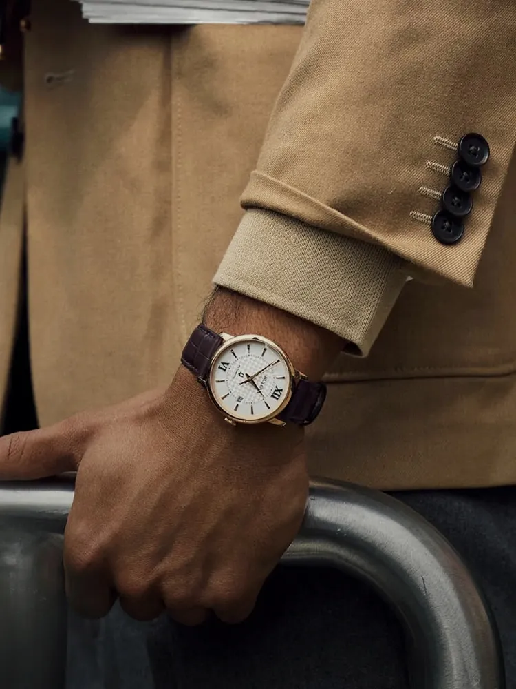 A close-up of a man's hand wearing a gold watch with a brown leather strap, resting on a railing.