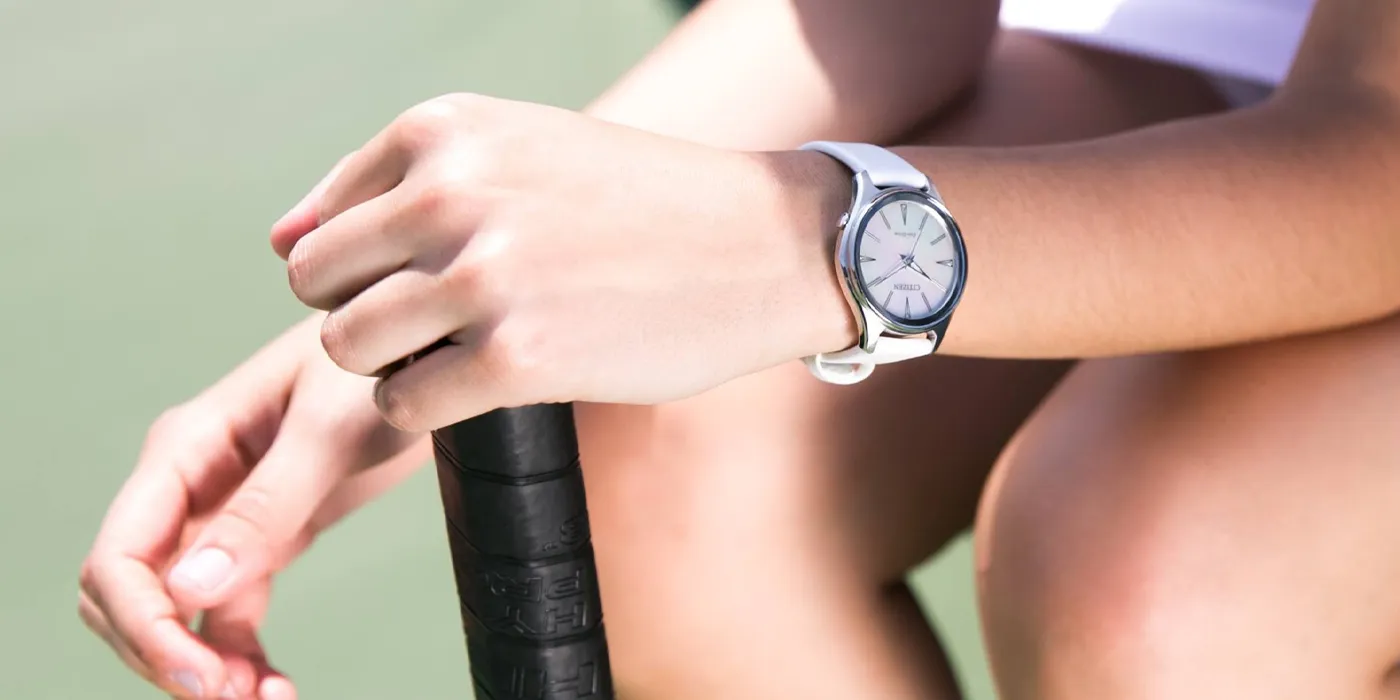 A close-up of a wrist wearing a white watch, holding a tennis racket, showcasing a sporty style.