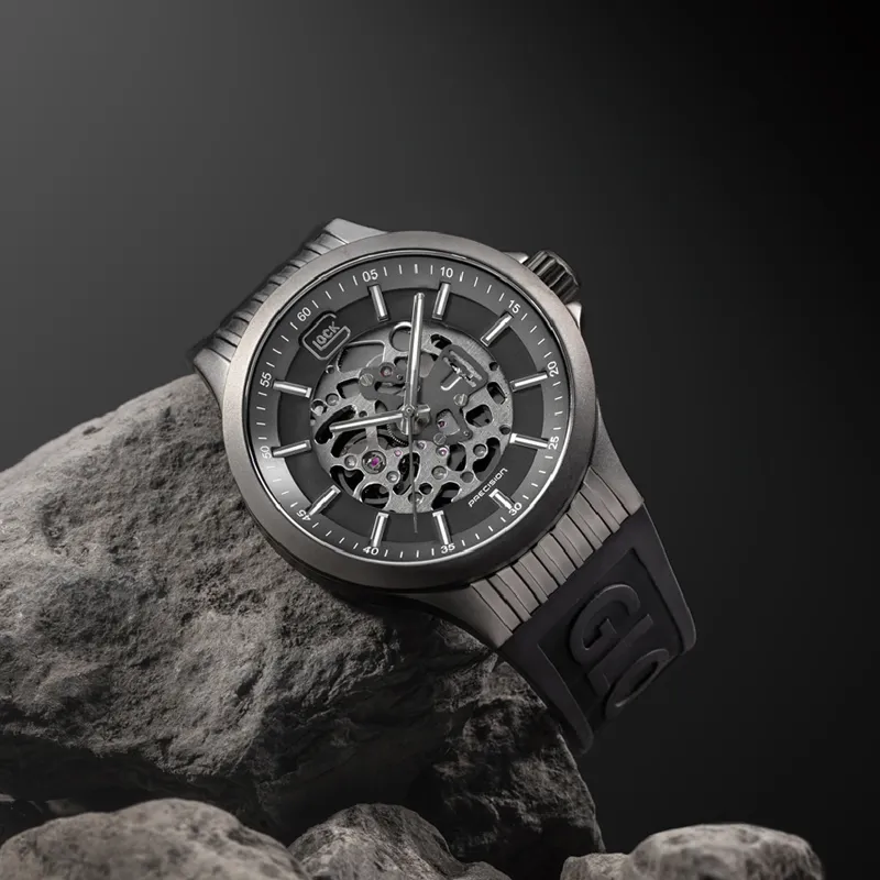 Stylish skeleton watch with a black strap, displayed on a rock against a dark background. Visit Bryan Jewelry for more.