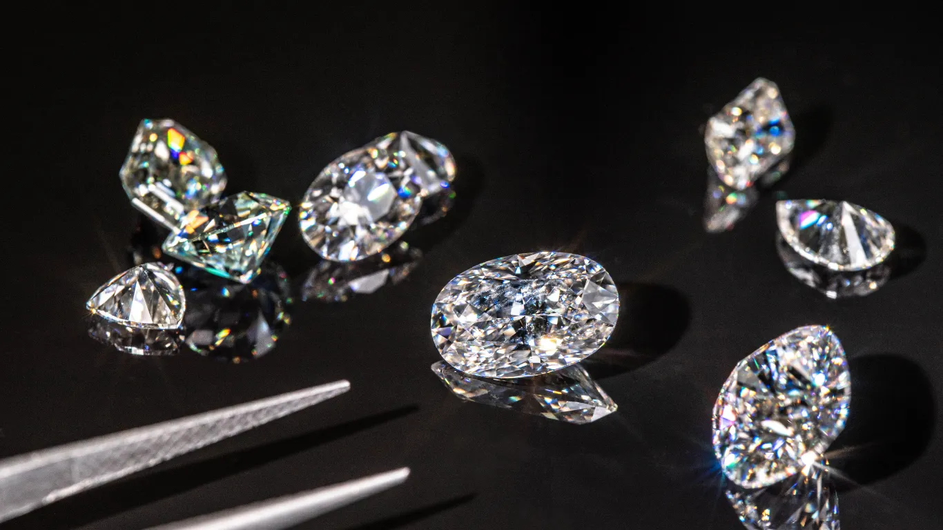 Sparkling diamonds on a reflective surface, with tweezers nearby. Explore services available at Buchkosky Jewelers.