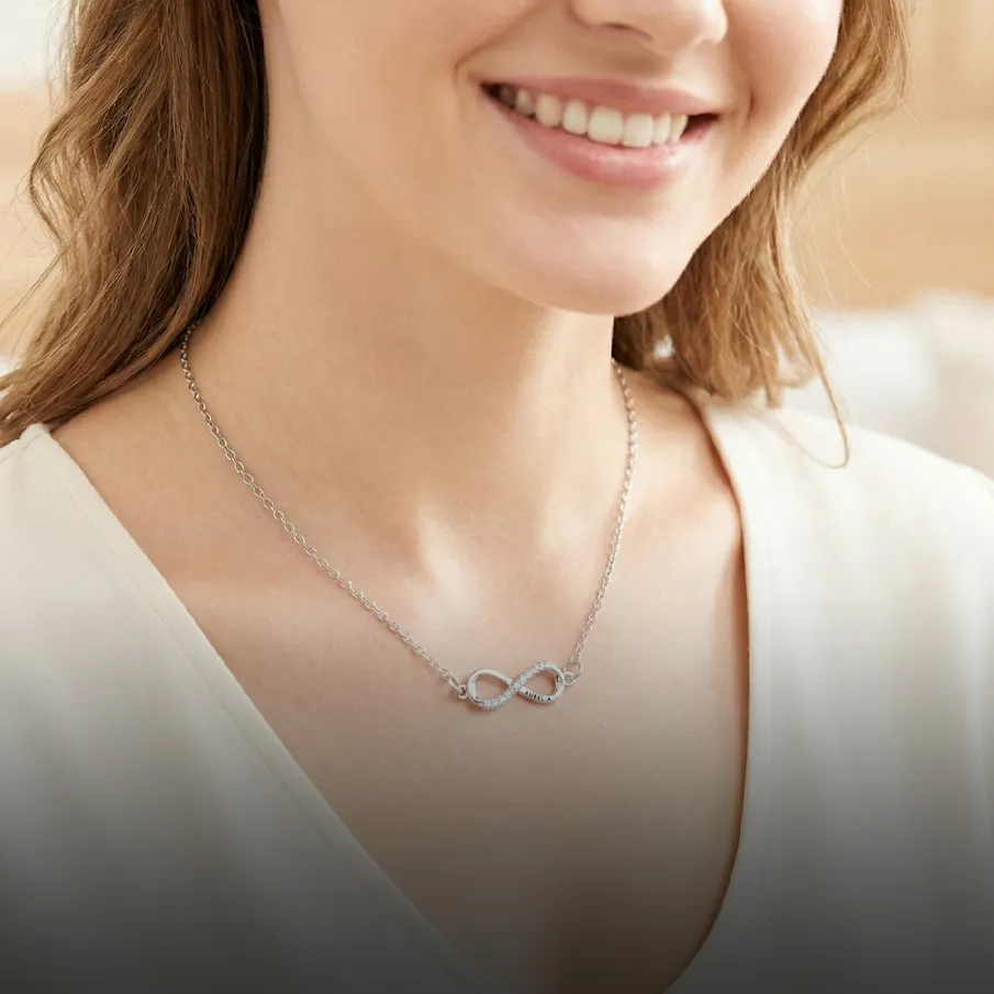 Woman wearing a silver infinity necklace, smiling.