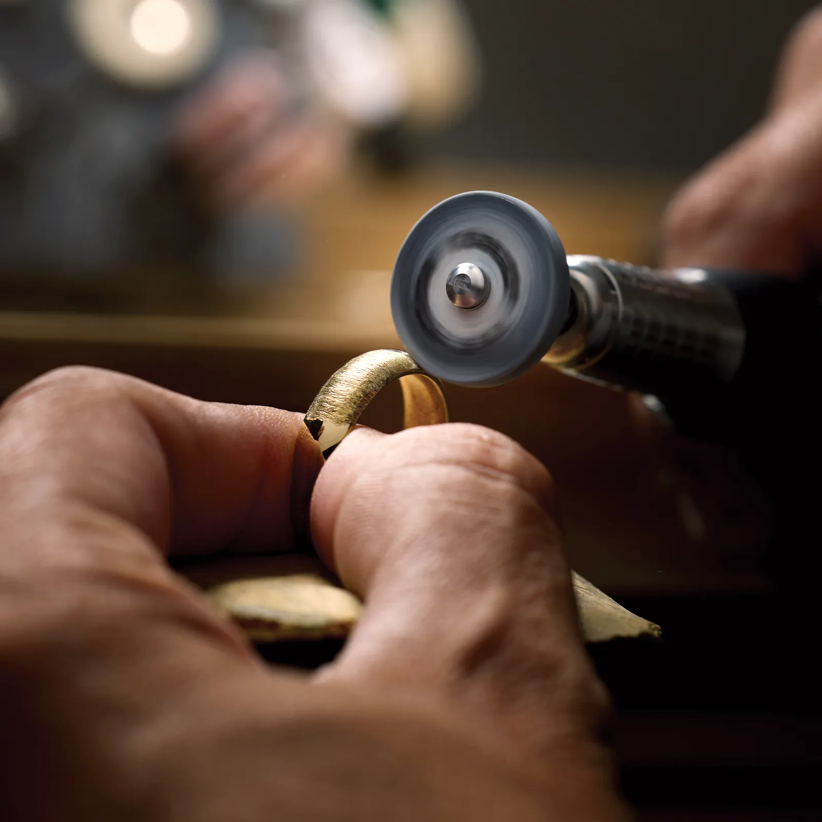 A person polishes a gold ring with a rotary tool, highlighting craftsmanship and precision.