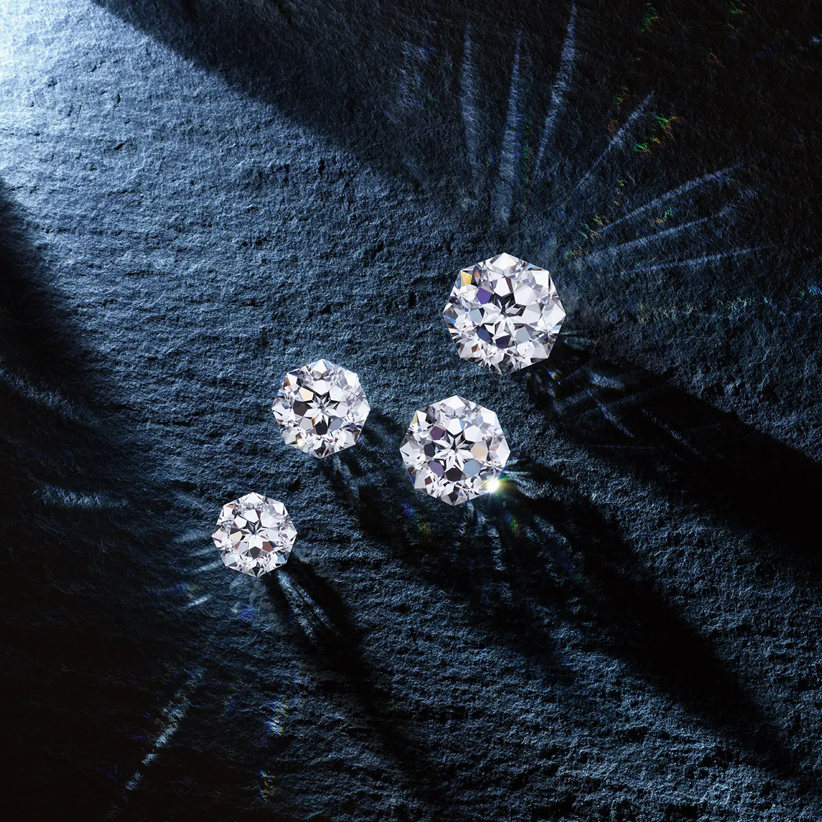 Four sparkling diamonds on a textured dark surface, showcasing brilliance and clarity.