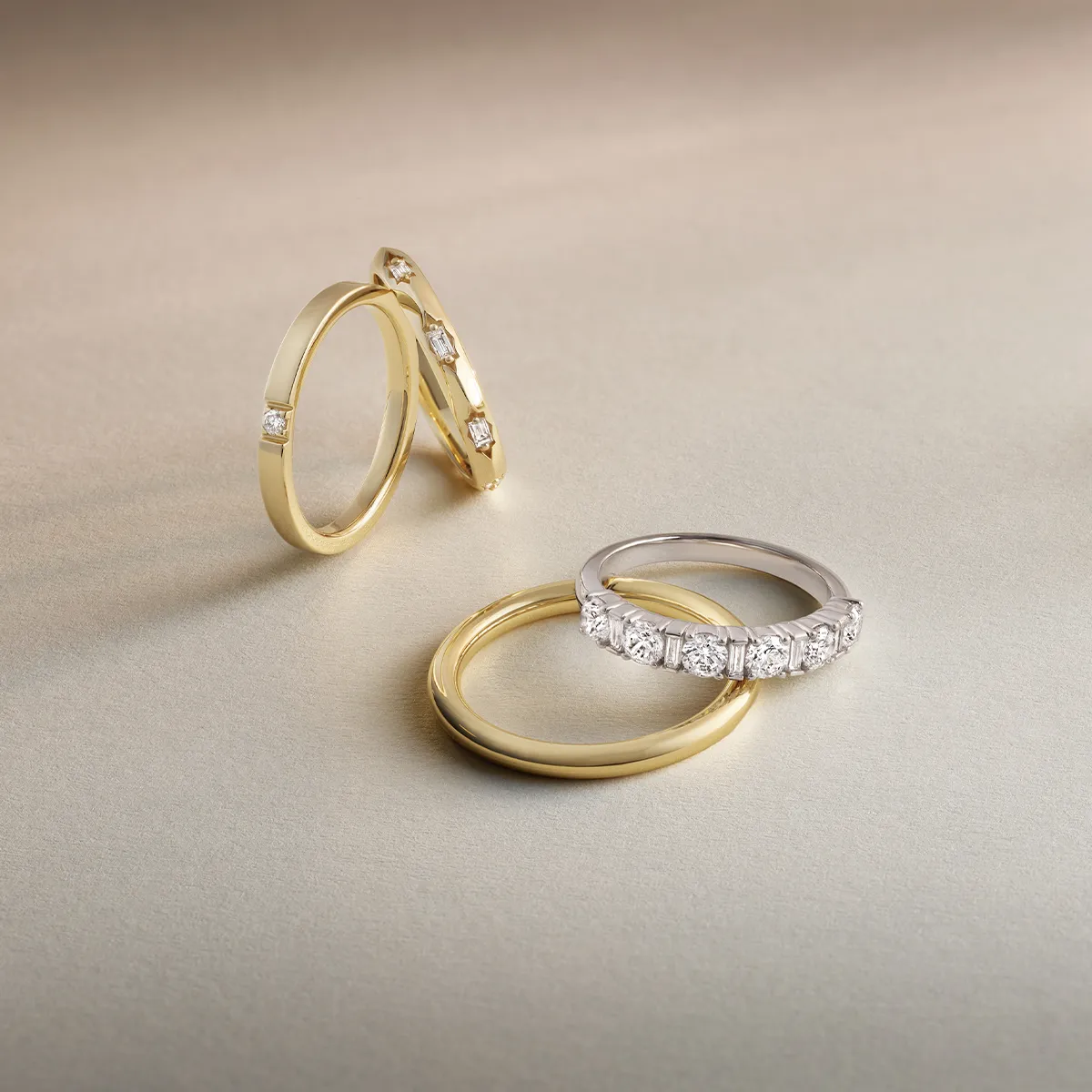 Three gold rings and one silver ring with diamonds on a beige surface.