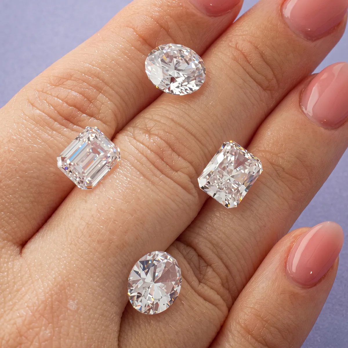 Four sparkling diamonds of different cuts displayed on a hand with manicured nails.