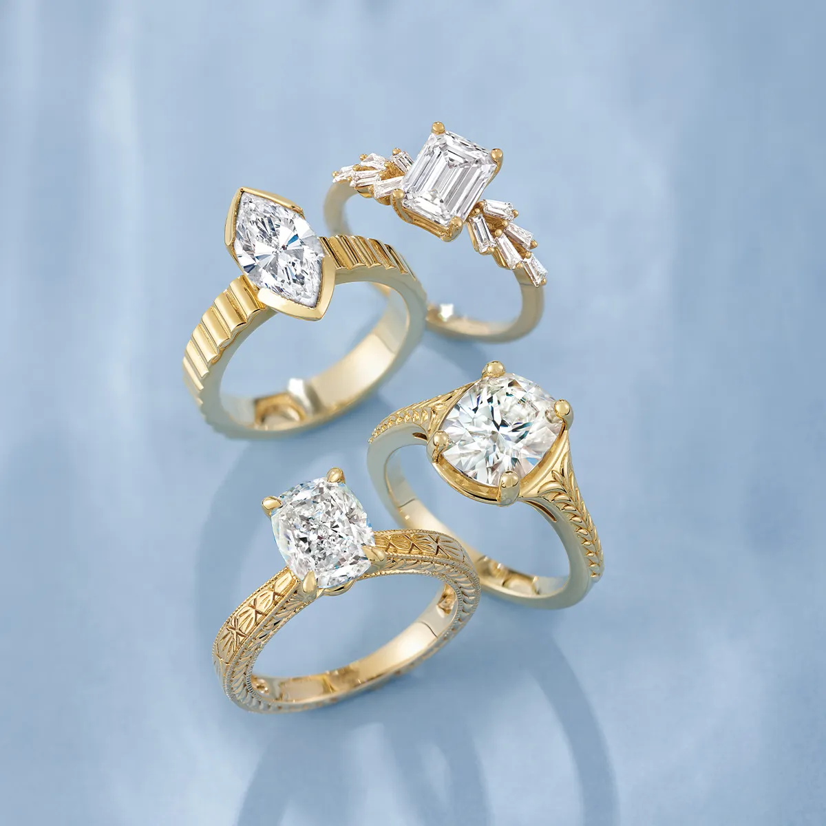 Four gold rings with various diamond cuts on a light blue background.