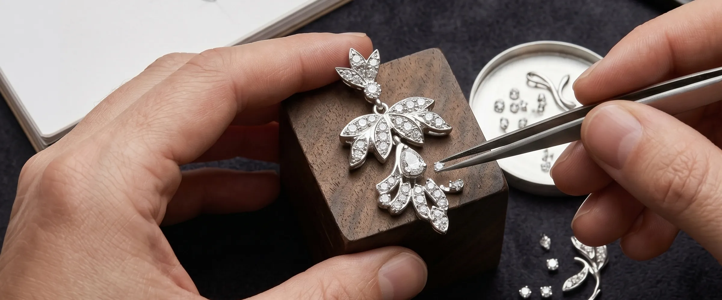 Jeweler setting diamonds in a leaf-shaped pendant with tweezers. Click to start a project at Canton Jewelry.