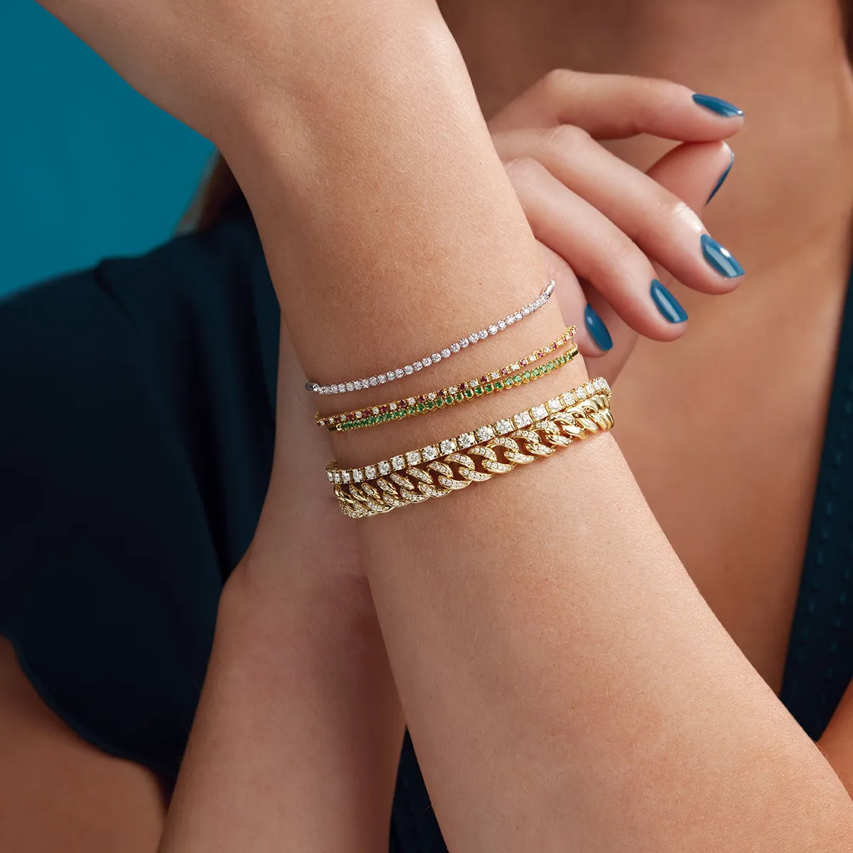 A woman's arm adorned with four elegant tennis bracelets in gold and silver tones.