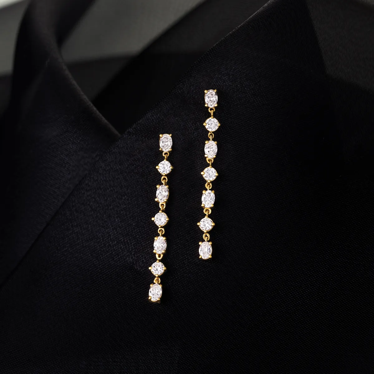 Elegant gold and diamond drop earrings on black fabric background.
