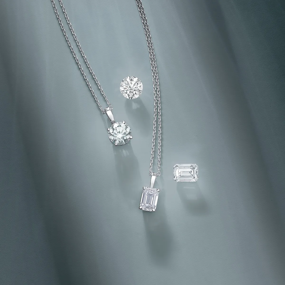 Elegant diamond necklaces and loose diamonds displayed on a soft gray background.