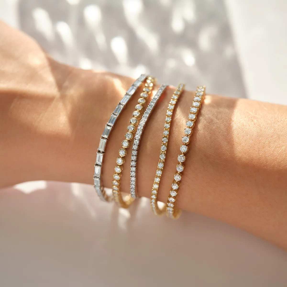 A wrist adorned with multiple diamond tennis bracelets in gold and silver settings.