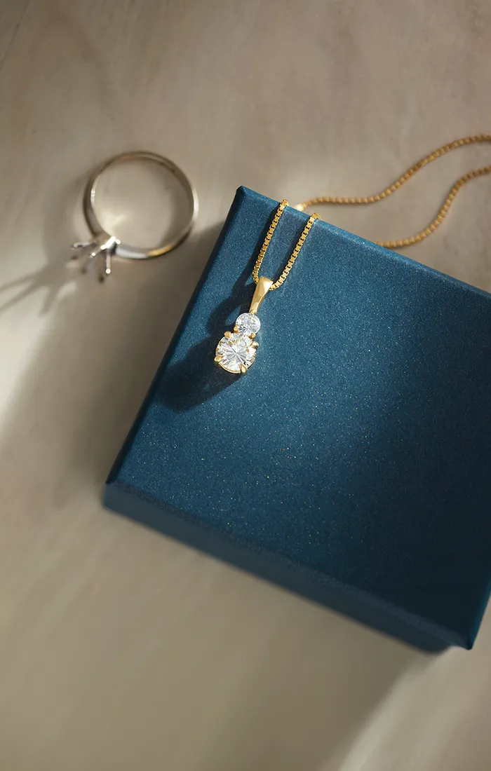 Gold pendant with diamonds on a blue box beside a ring setting on a light surface.