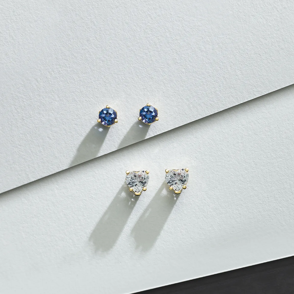 Two pairs of stud earrings: blue gemstones and clear diamonds on a textured white surface.