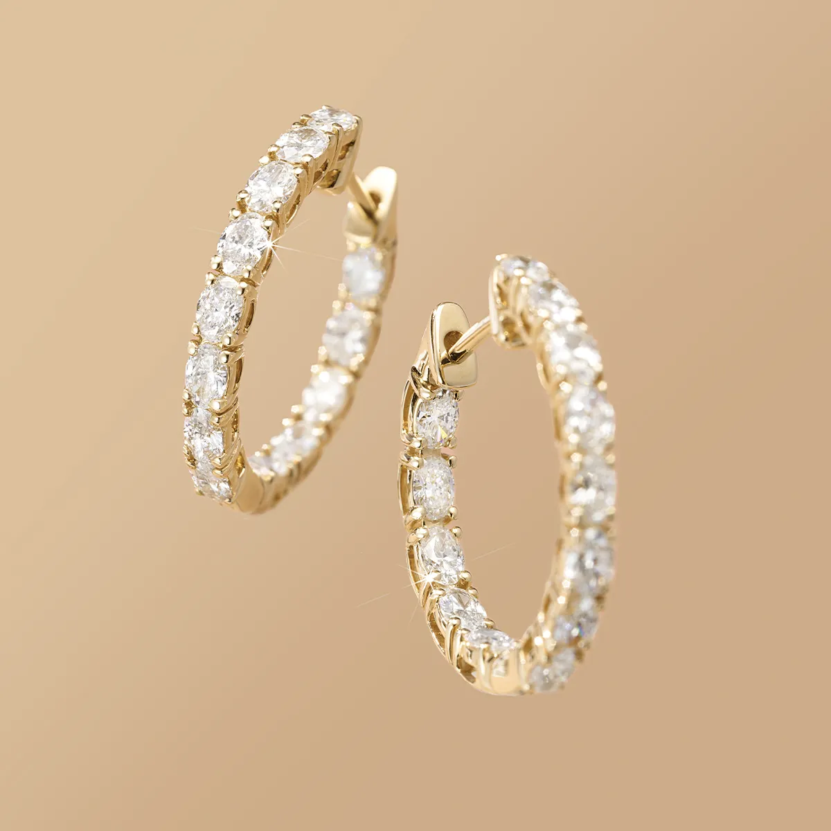Gold hoop earrings with sparkling diamonds on a beige background.