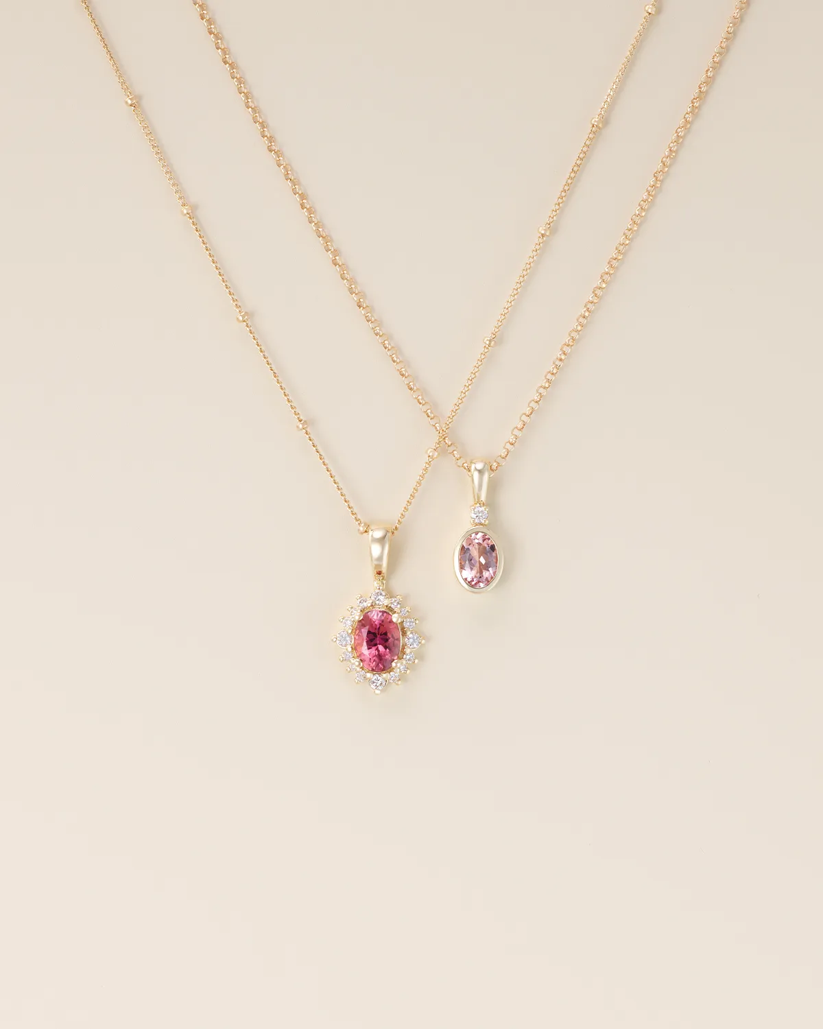 Two gold necklaces with pink gemstone pendants on a beige background. Shop Now.