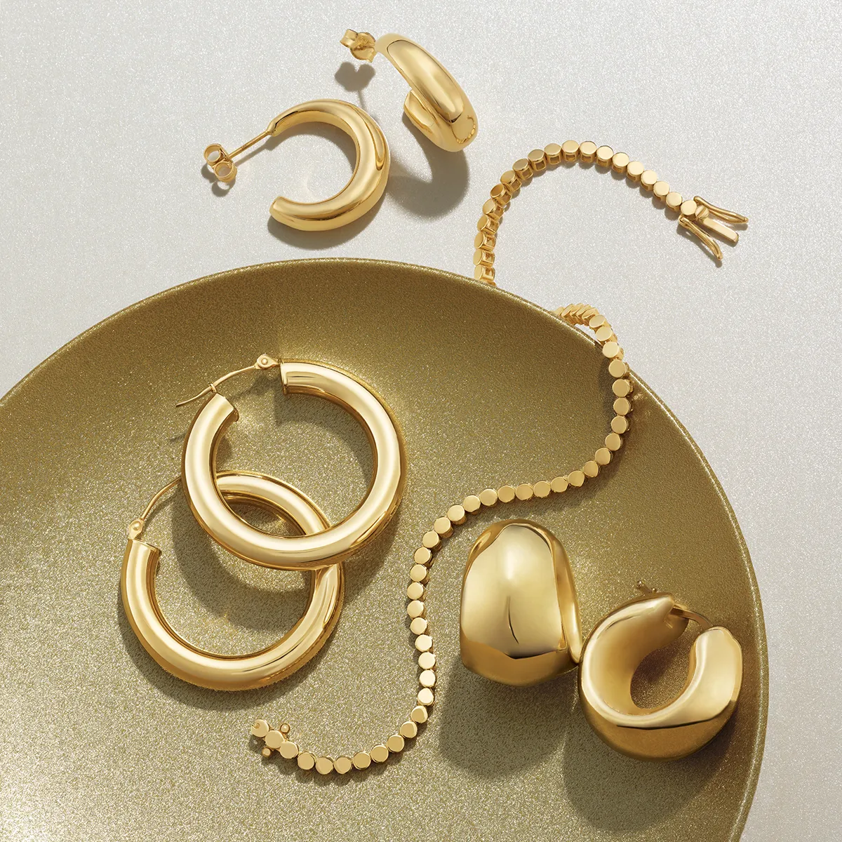 Gold hoop earrings and bracelet displayed on a shimmering surface.