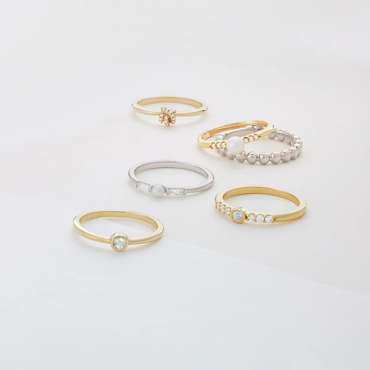 A collection of elegant stackable rings in gold and silver with various gemstones on a light background.