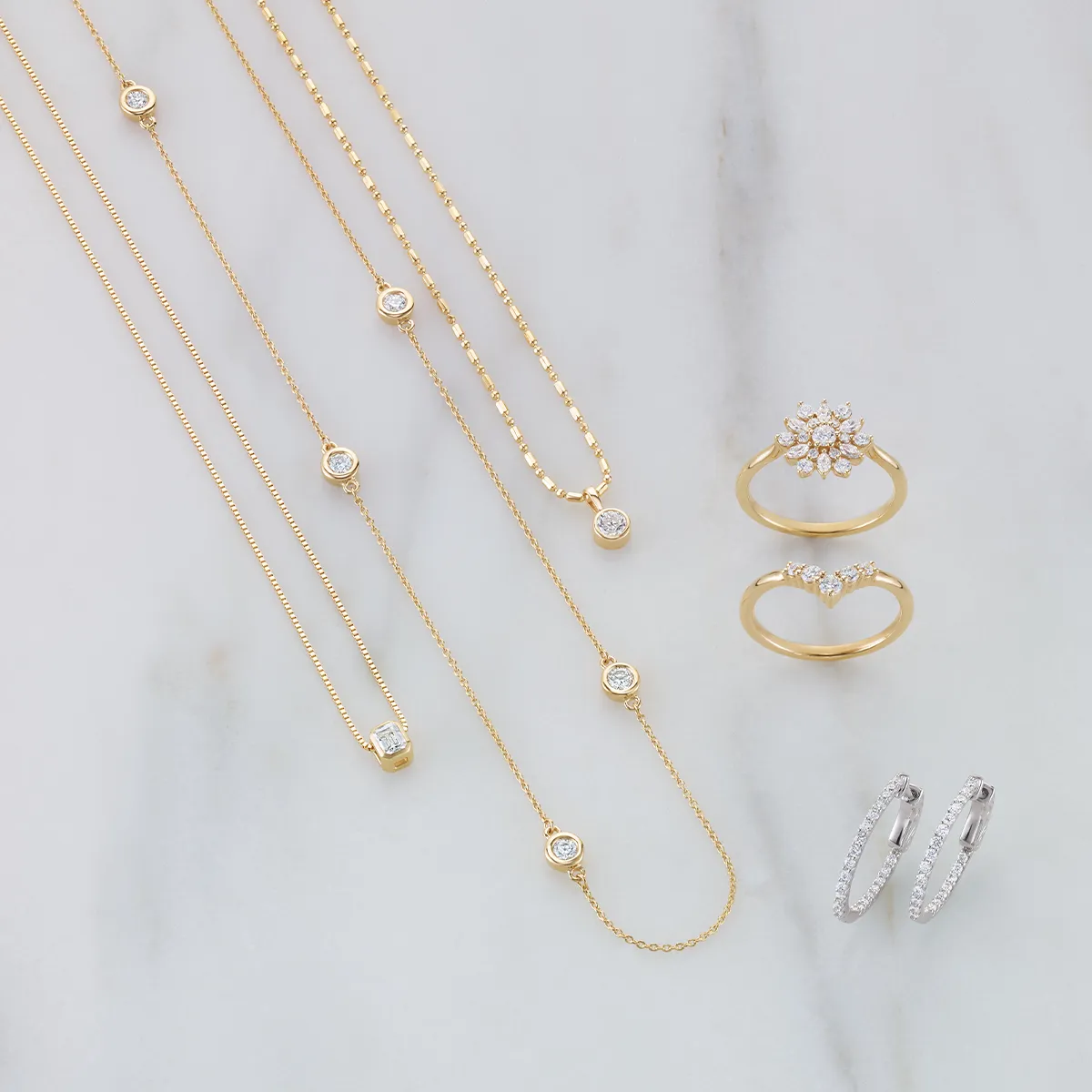 Gold necklaces, rings, and silver hoop earrings displayed on a marble surface.