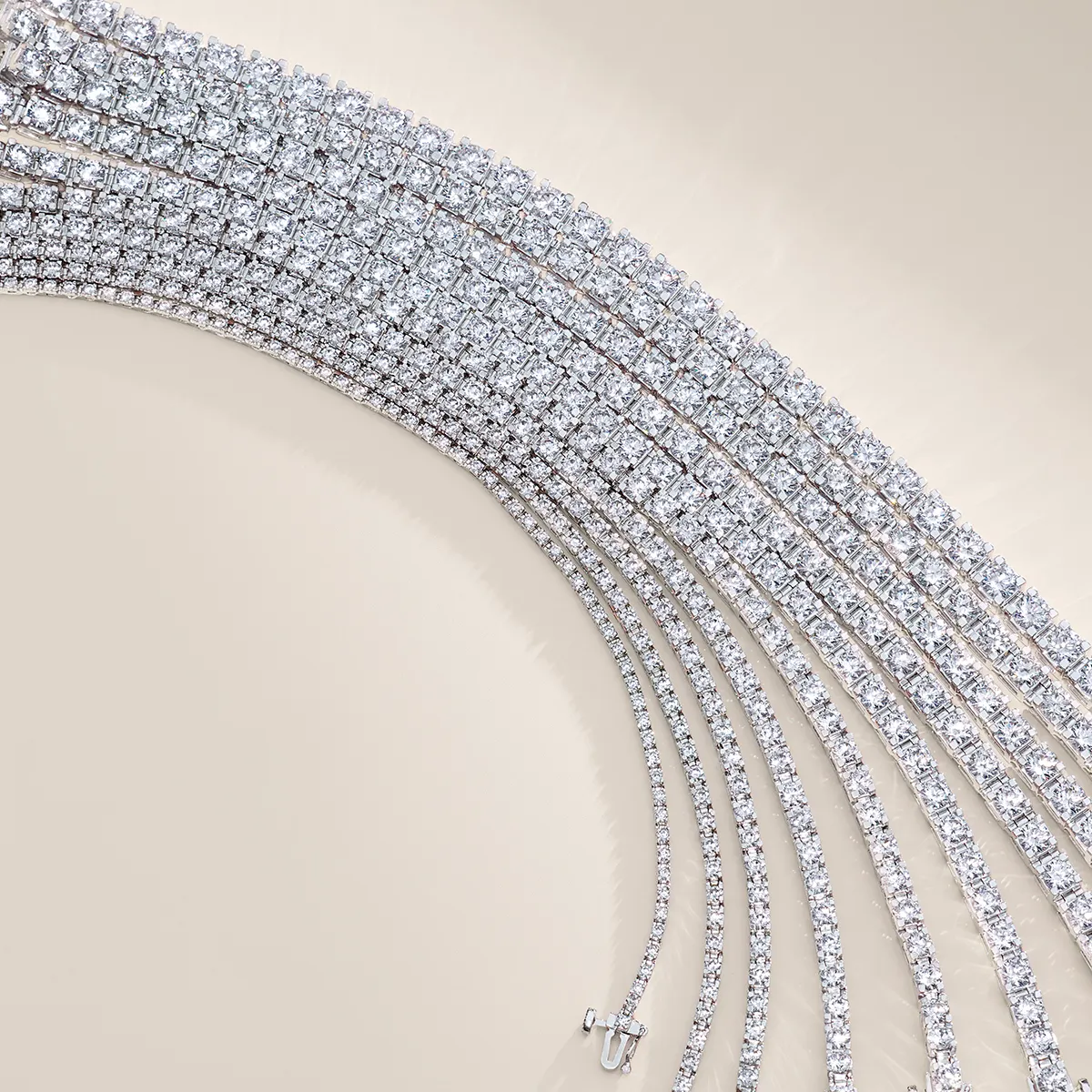 Elegant diamond tennis bracelets displayed in a curved arrangement on a beige background.