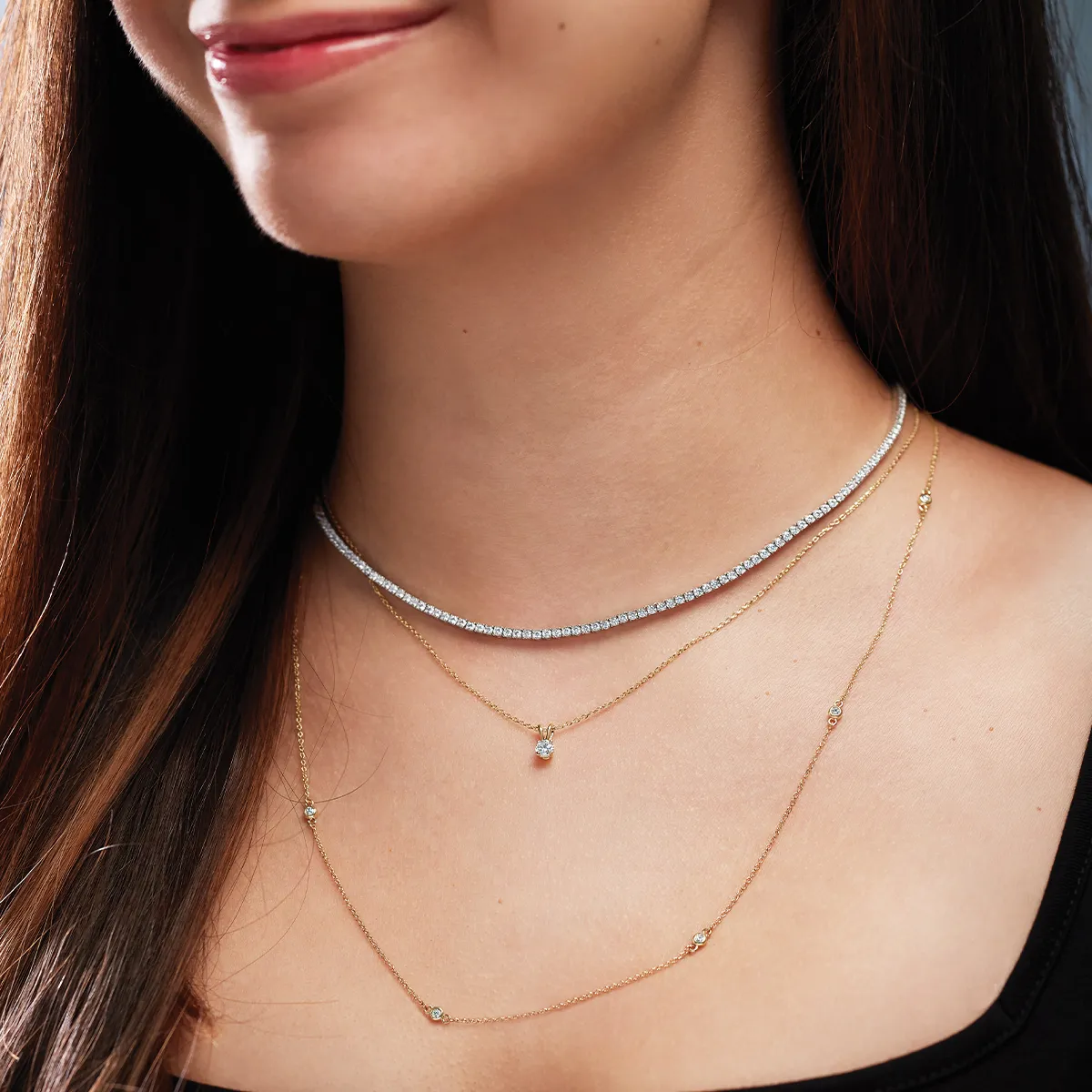 Close-up of a woman wearing layered necklaces, including a diamond tennis necklace.