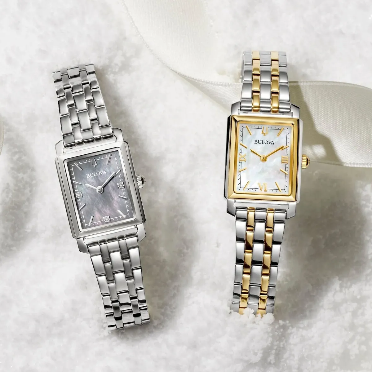 Two Bulova watches with metal bands on a snowy surface, one silver and one two-tone.