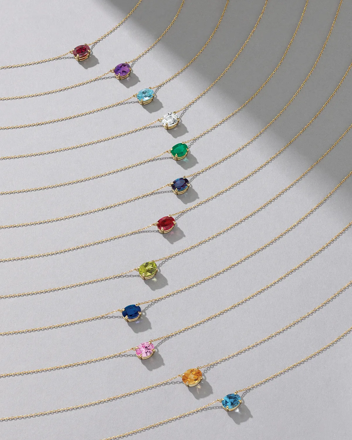 Gold necklaces with colorful gemstone pendants arranged in a diagonal pattern. Shop Now.