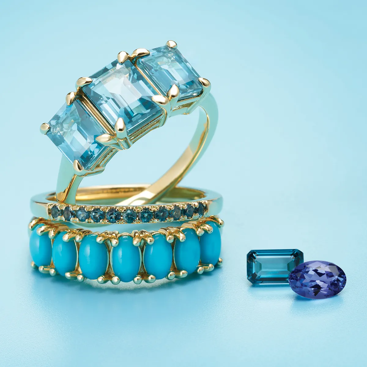 Three gold rings with blue gemstones and two loose gemstones on a blue background.