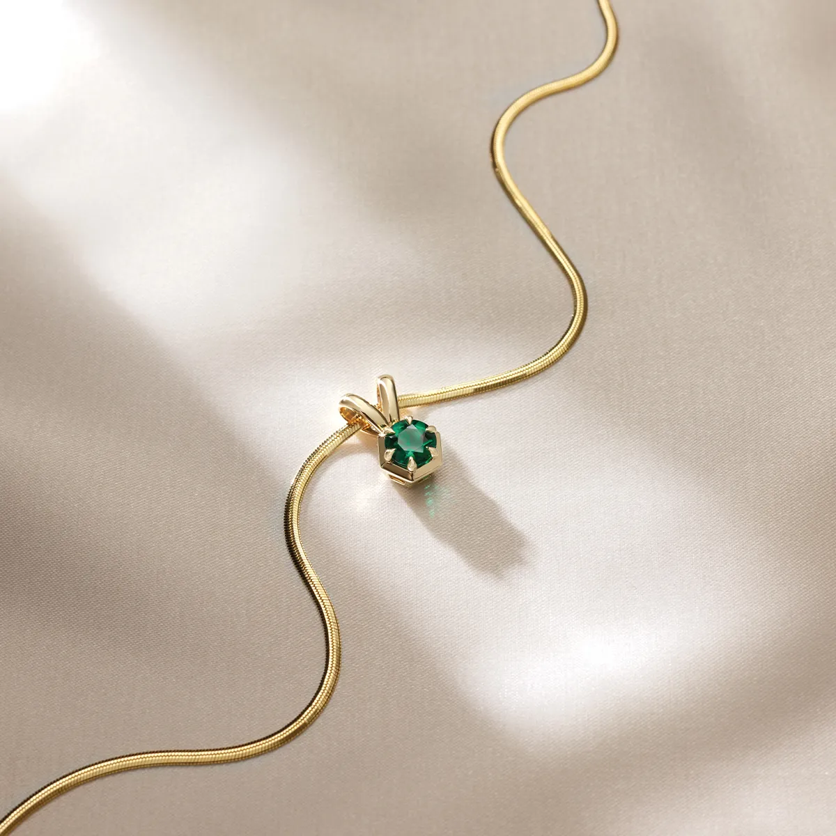 Elegant gold necklace with emerald pendant on silky fabric background.