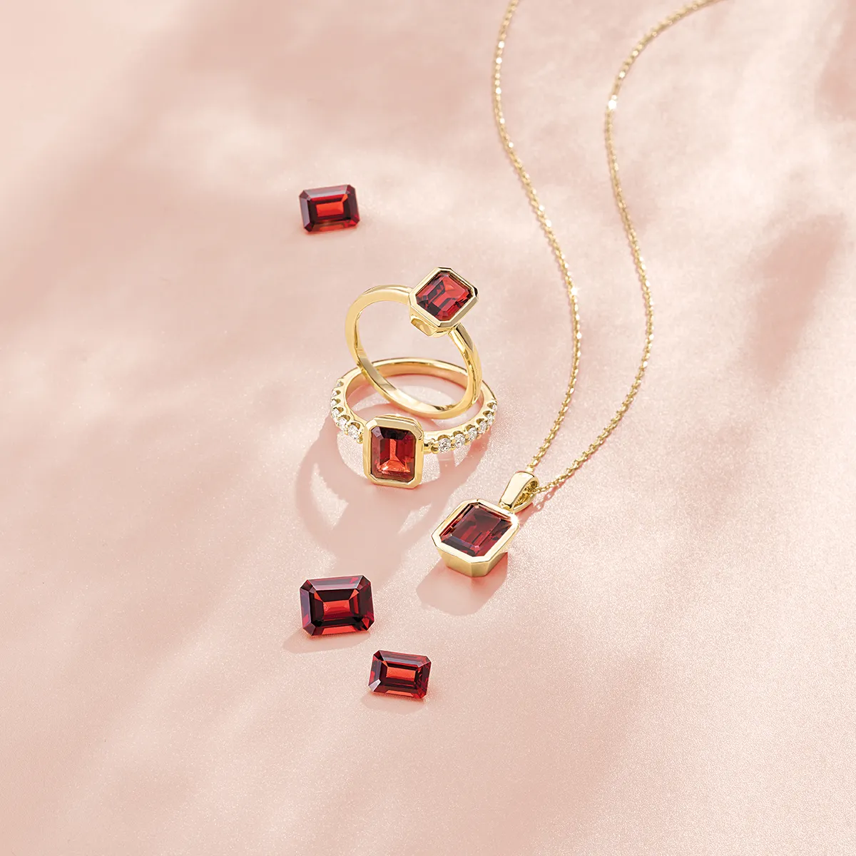 Gold rings and necklace with red garnet stones on a pink satin background.