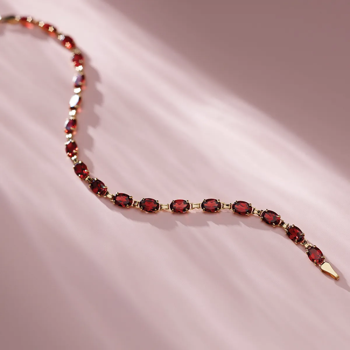 Elegant bracelet with red gemstones on a soft pink background.