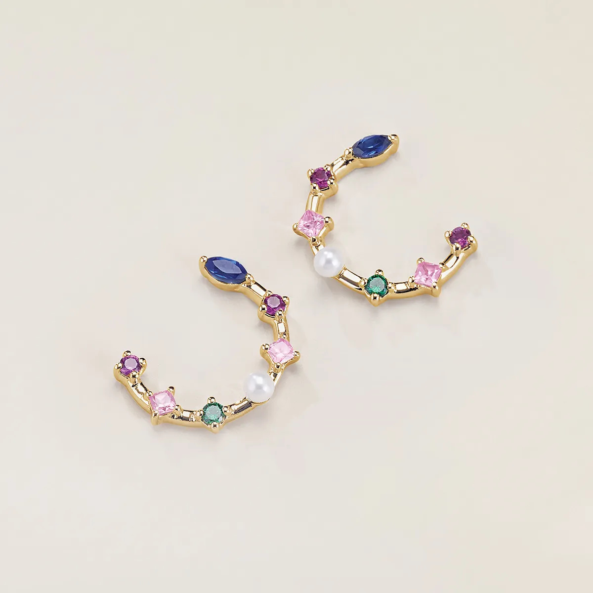 Colorful gemstone earrings with pearls and gold setting on a light background.