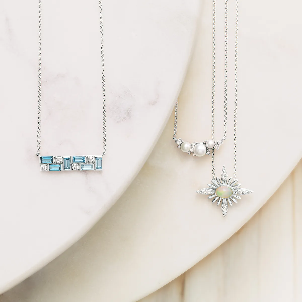 Three elegant gemstone necklaces displayed on a marble surface.