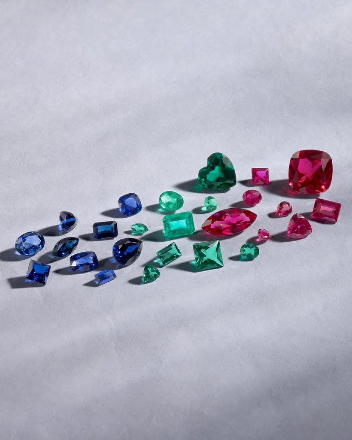 Loose gemstones in blue, green, and red on a light surface. Shop Now.