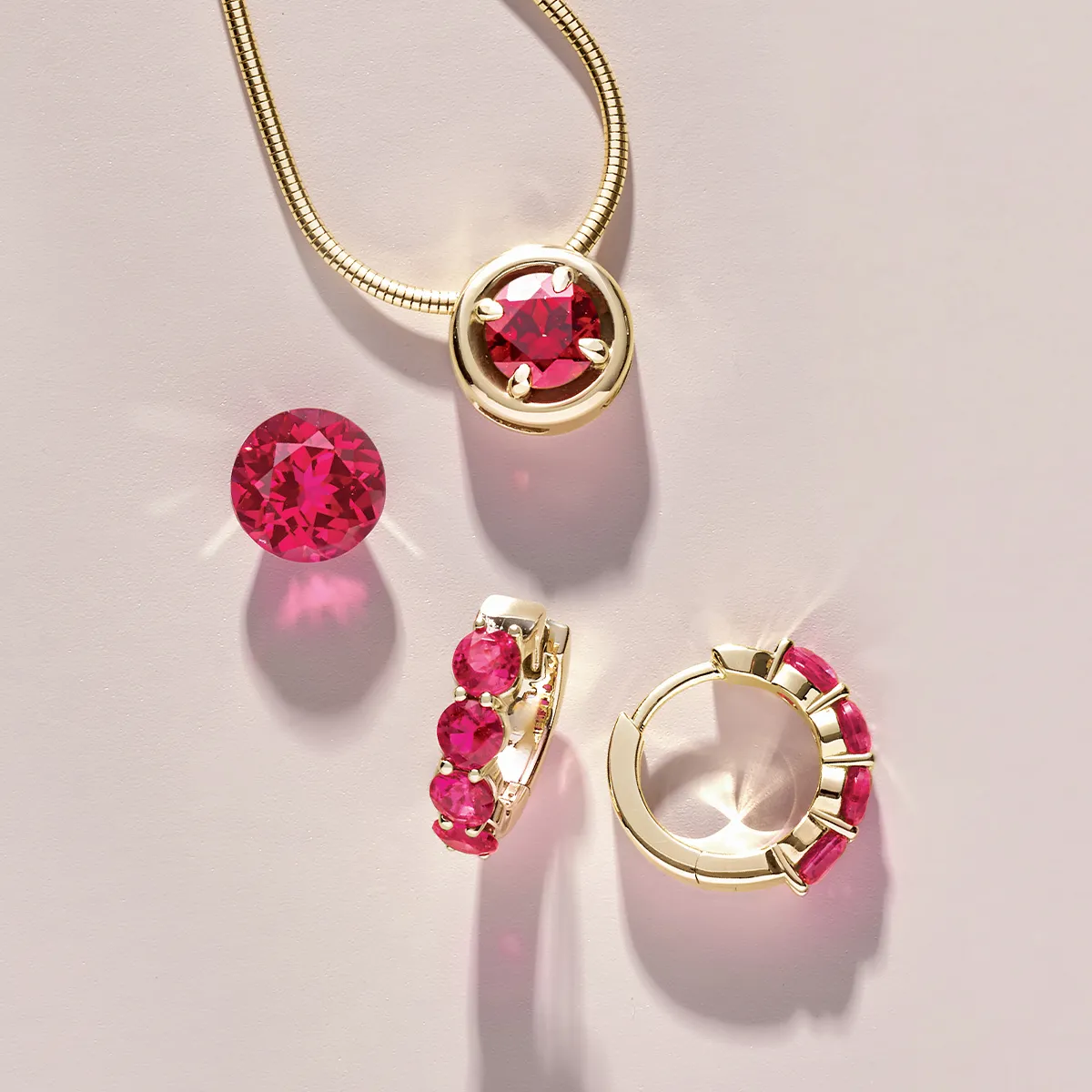Gold jewelry set with vibrant pink gemstones, including a necklace and earrings, on a light background.