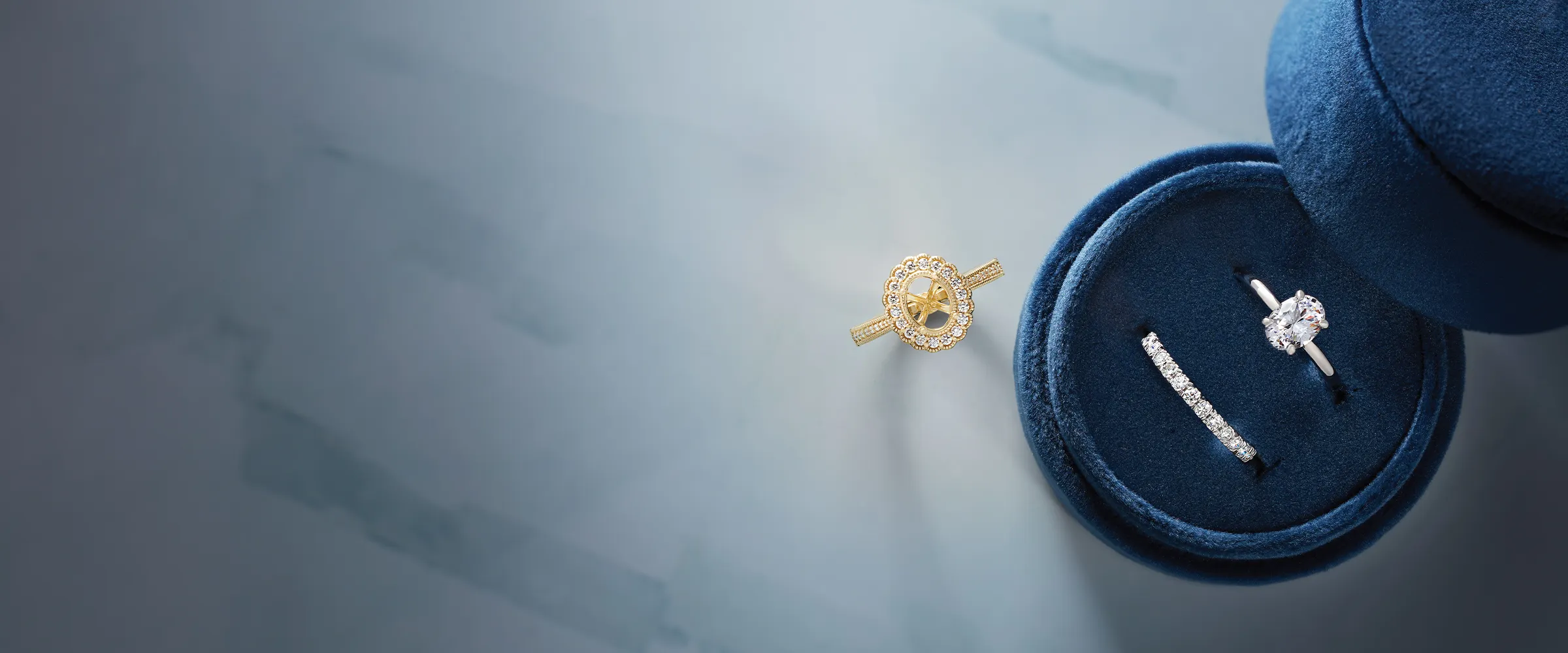 Jewelry pieces displayed on a blue velvet box, including a diamond ring and a gold ring setting.