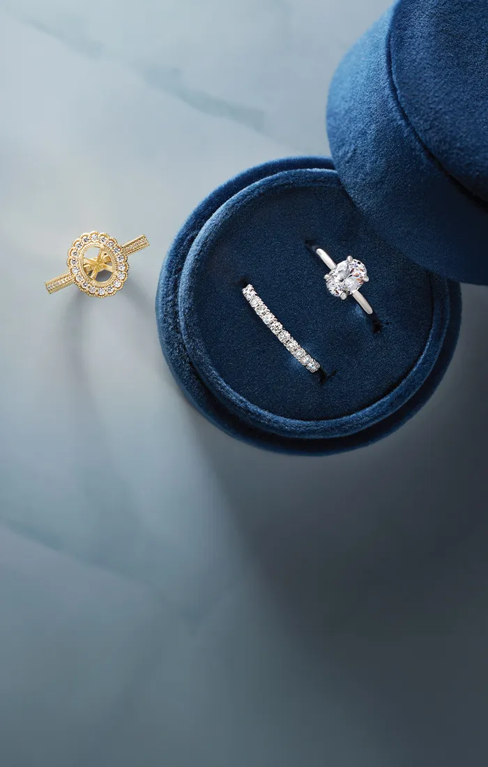 Jewelry pieces displayed on a blue velvet box, including a diamond ring and a gold ring setting.