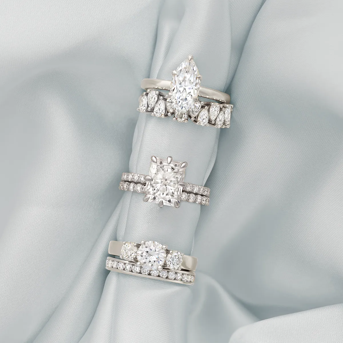 Three elegant engagement rings with different diamond cuts on a soft fabric background.