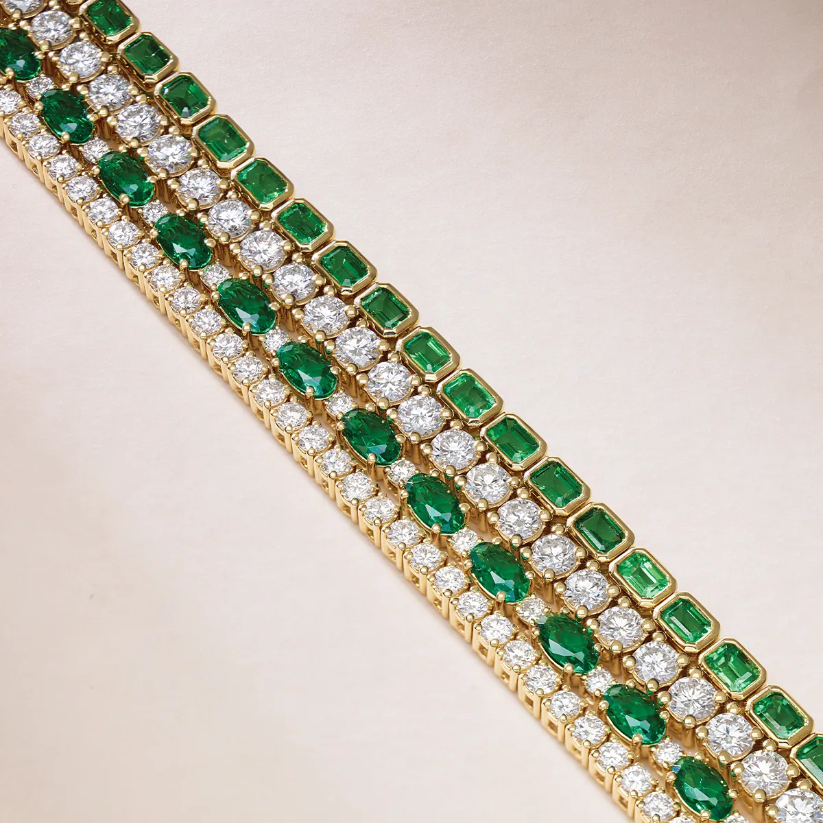 Elegant gold bracelet with emerald and diamond rows on a light background.