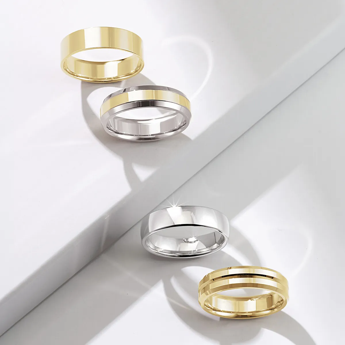 Four wedding bands in gold and silver displayed on a white surface.