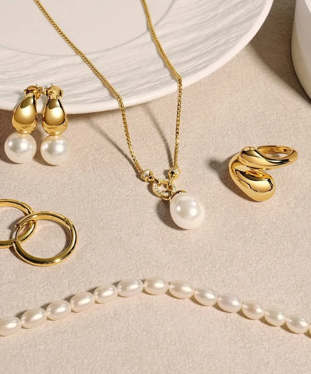 Gold jewelry with pearls, including earrings, necklace, rings, and a pearl strand, displayed on a beige surface.