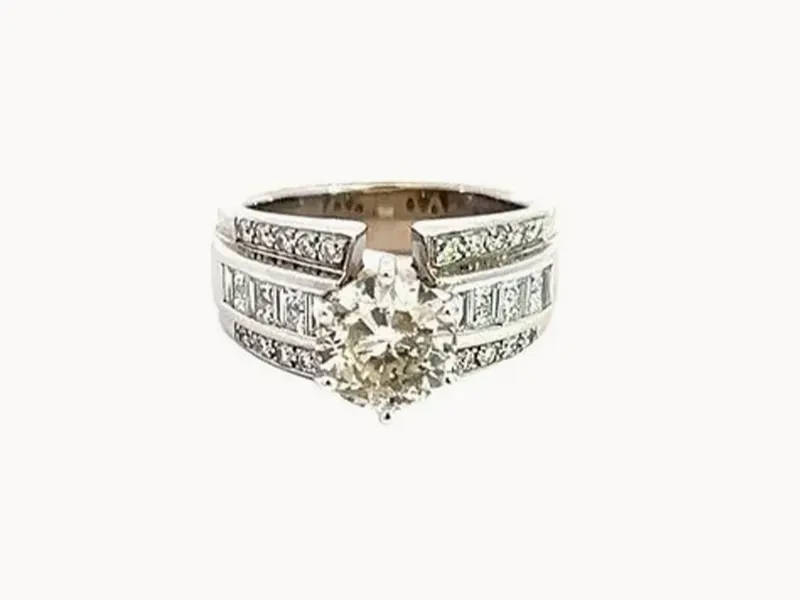 A diamond ring with a round center stone and a split shank encrusted with smaller diamonds.