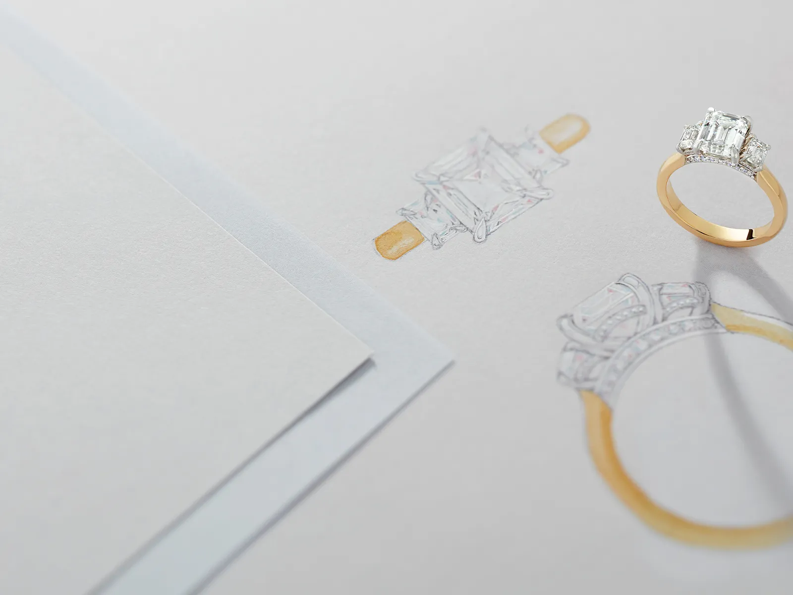 A gold engagement ring with a large diamond next to its sketch on paper.